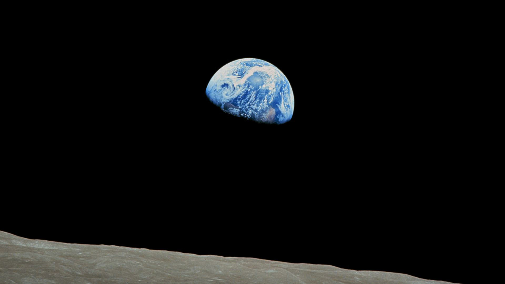 Earthrise: the Earth suspended in black space above the grey lunar horizon, as photographed by Apollo astronauts.