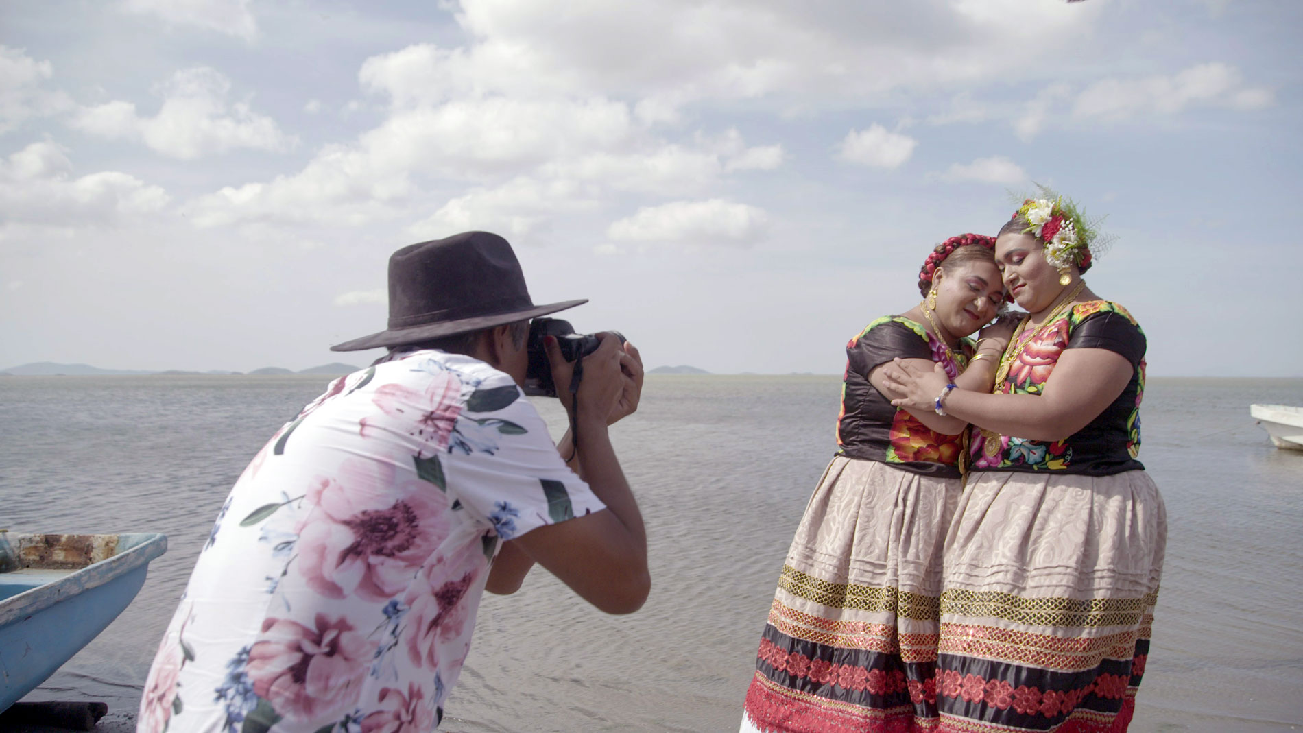 A photographer captures two women in traditional Zapotec dress embracing on a lakeshore.